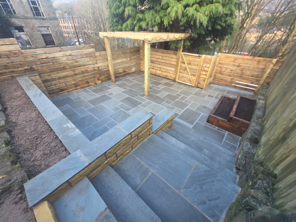 Stone patio with timber pergola and raised sleeper planters
