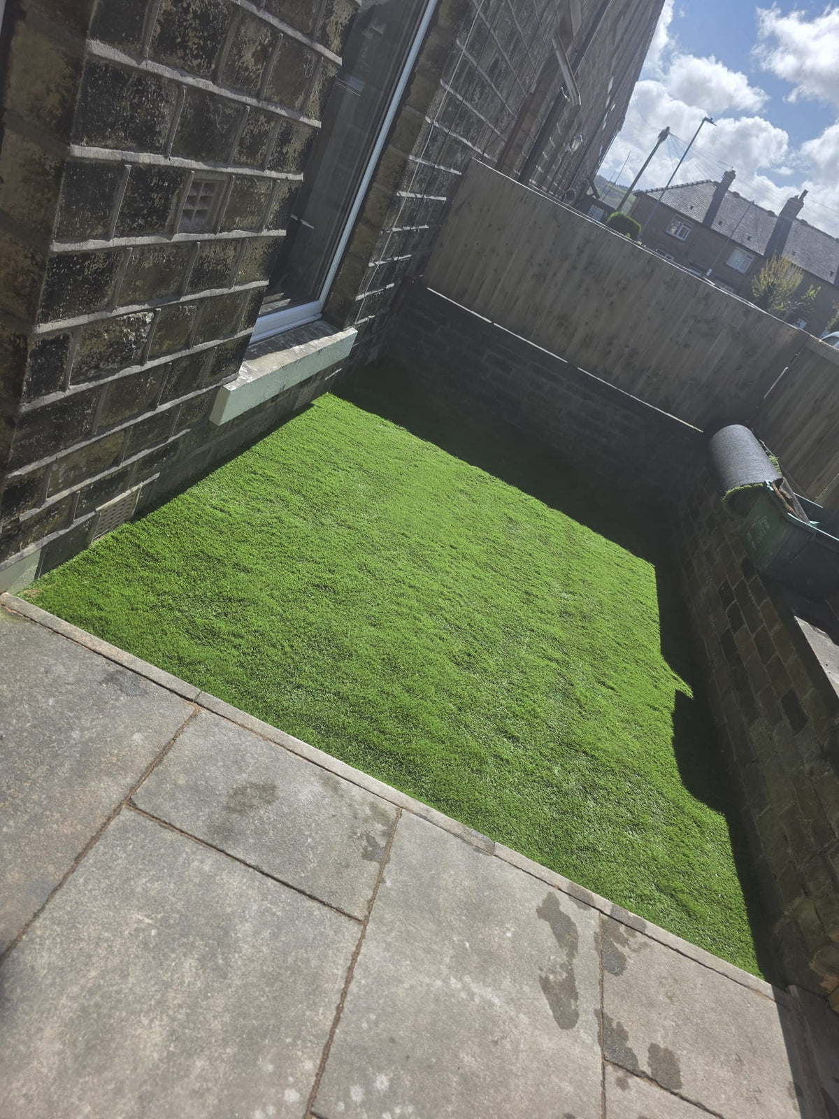 Small grass area beside a stone house and paving