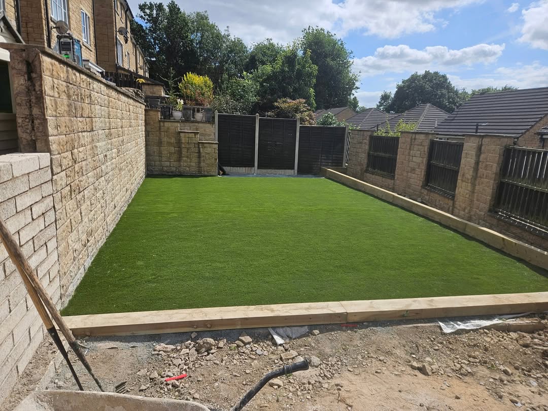 Artificial grass with timber edging beside a stone wall